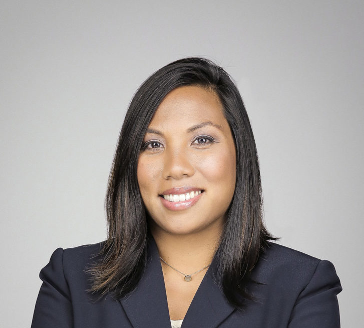 Headshot of April Veneracion. She wears a business suit and has her arms folded.